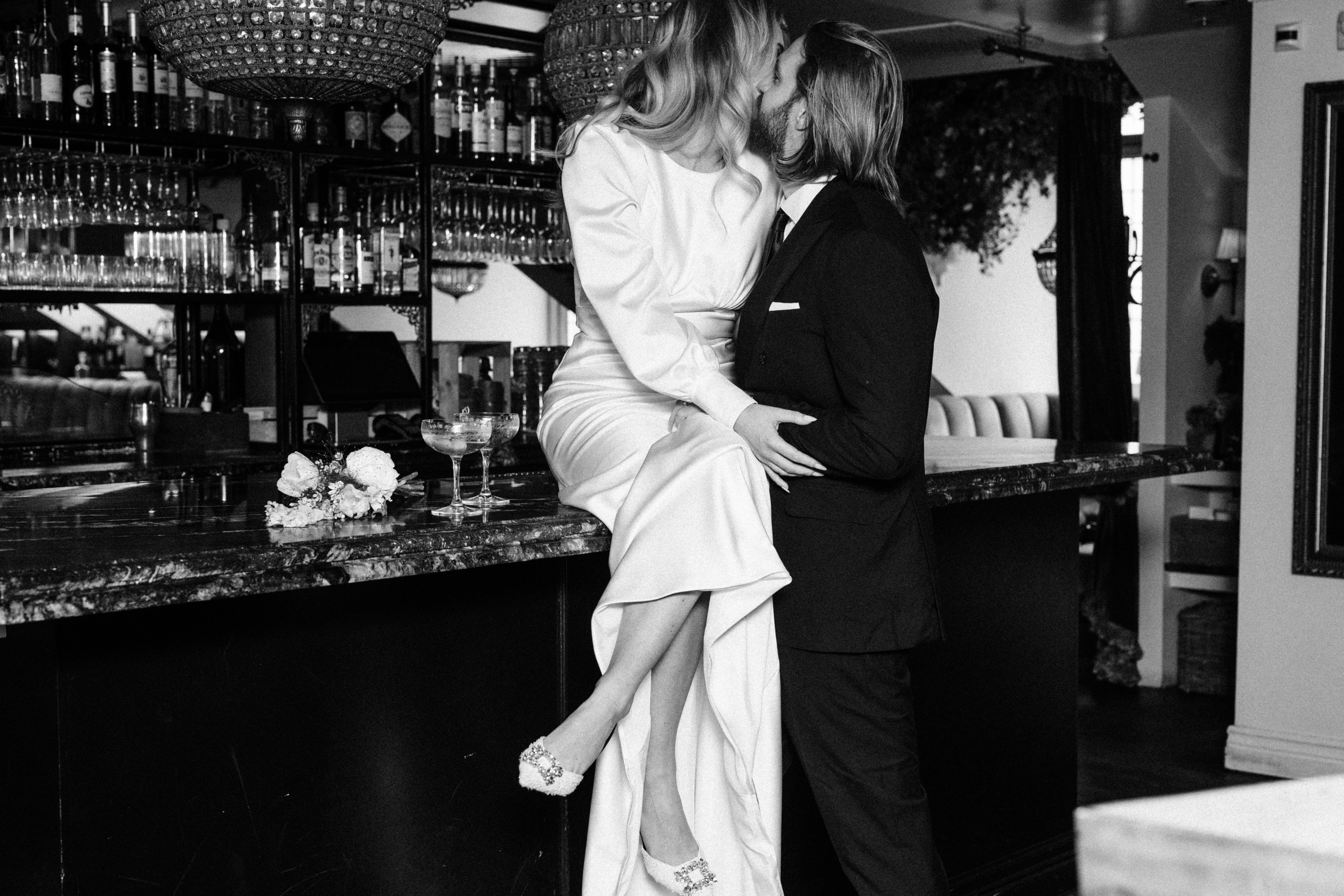 Bröllop Bar Pigalle Göteborg Brudpar kysser vid marmorbaren på Bar Pigalle i Göteborg med champagneglas och blombukett